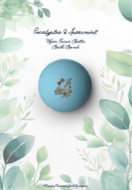 Top-down of pale blue-green spherical Eucalyptus & Spearmint Oat Milk Bath Bomb, set within a botanical border by Happy Hummingbird Soapery.