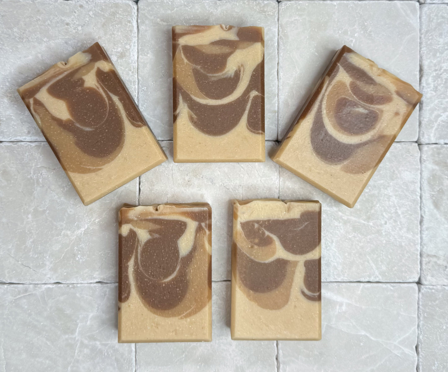 Palo Santo handmade soap bars arranged on a light stone tile background with warm beige and brown swirl pattern