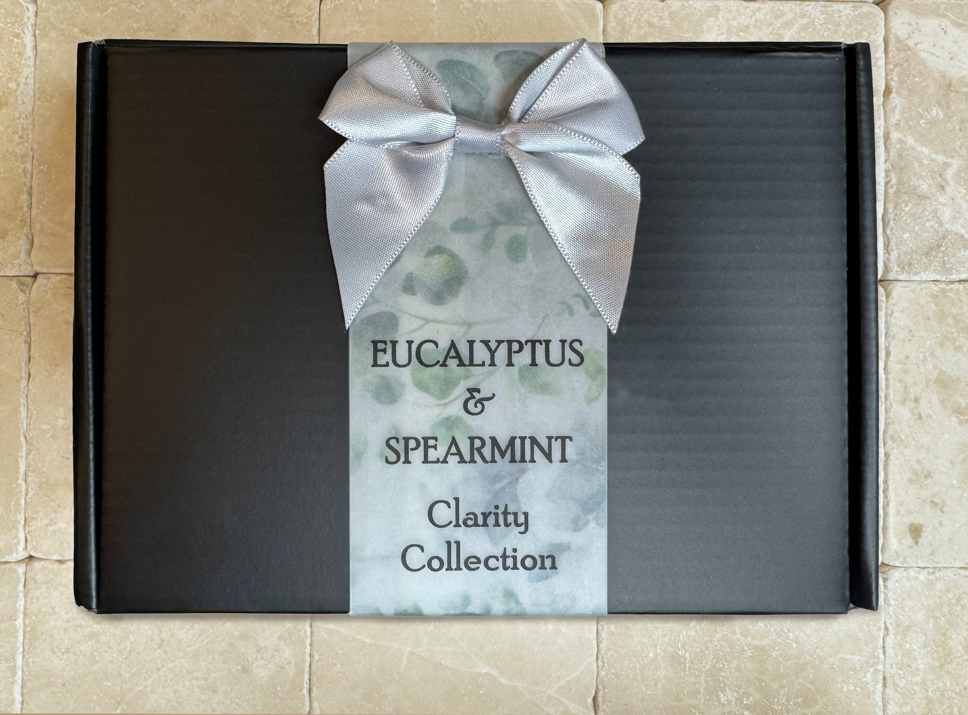 Premium black gift box from the Eucalyptus & Spearmint Collection, sitting on a natural travertine stone surface.