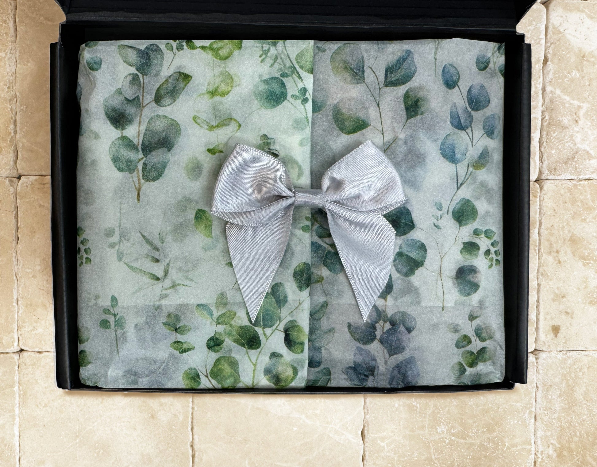 Eucalyptus & Spearmint premium gift box with leaf tissue paper covering bath products, resting on a travertine stone surface.