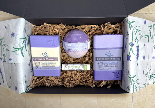 Happy Hummingbird Soapery Lavender Harmony gift set in an open black box, featuring 2 artisan soap bars, a round bath bomb, and a peppermint nourishing lip balm, arranged on recycled brown crinkle paper.