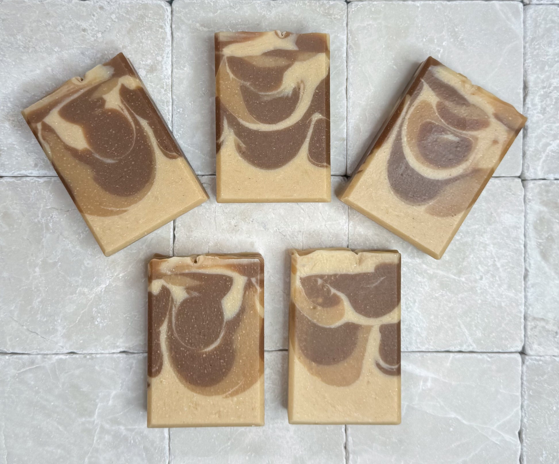 Palo Santo handmade soap bars arranged on a light stone tile background with warm beige and brown swirl pattern
