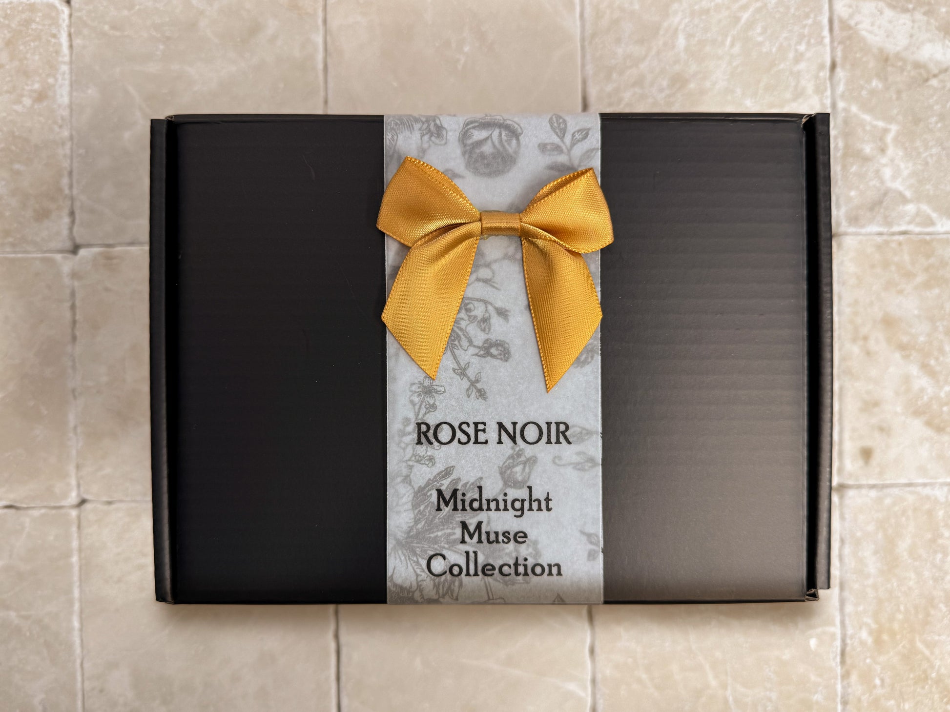 Premium black gift box from the Rose Noir Midnight Muse Collection, sitting on a natural travertine stone surface.