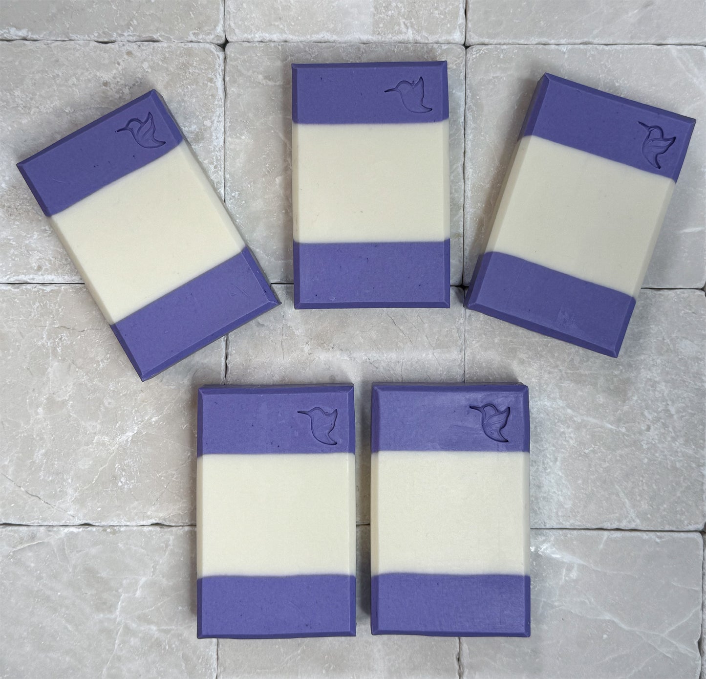 Multiple handcrafted Lavender Morning vegan soap bars by Happy Hummingbird Soapery arranged on a neutral stone surface, highlighting the clean, artisan layered design.