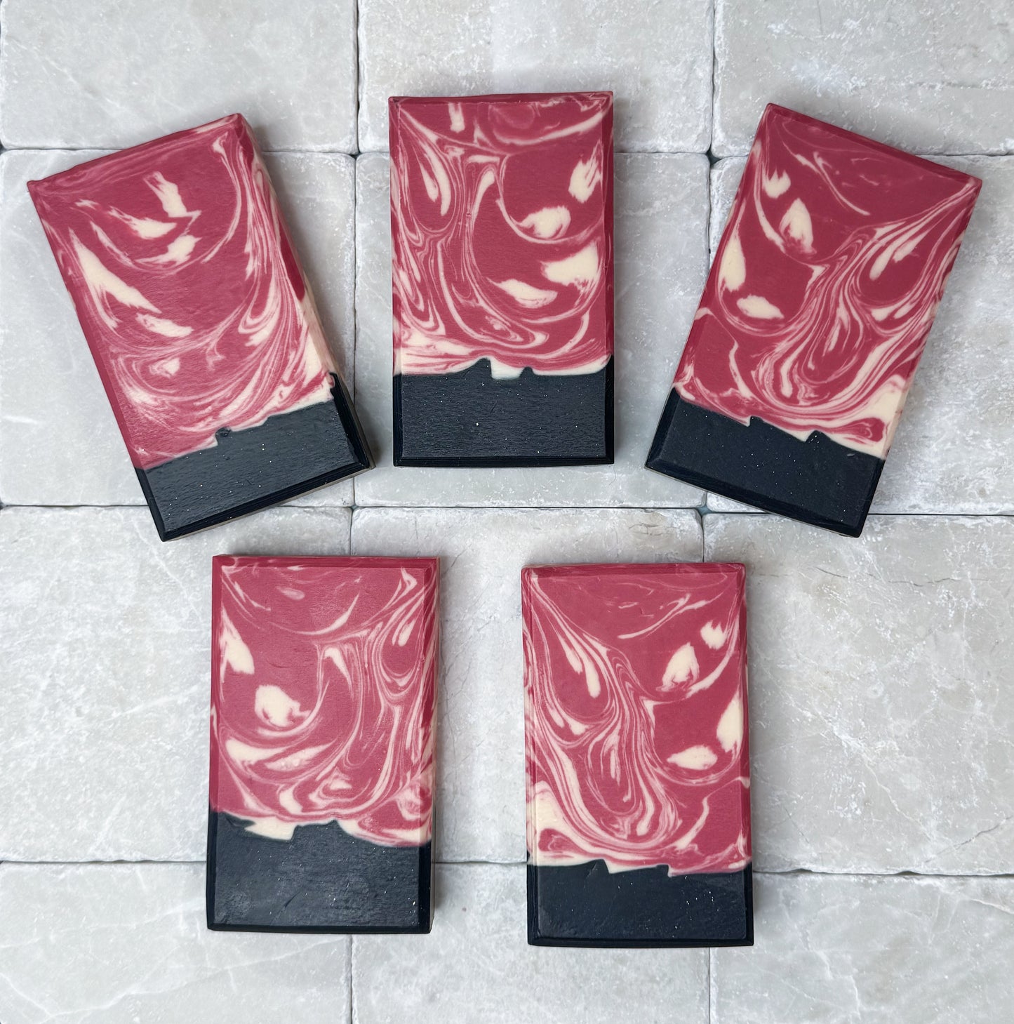 Rose Noir by Happy Hummingbird Soapery: Five rectangular bars with deep red and black marble swirls arranged on a neutral light stone surface.