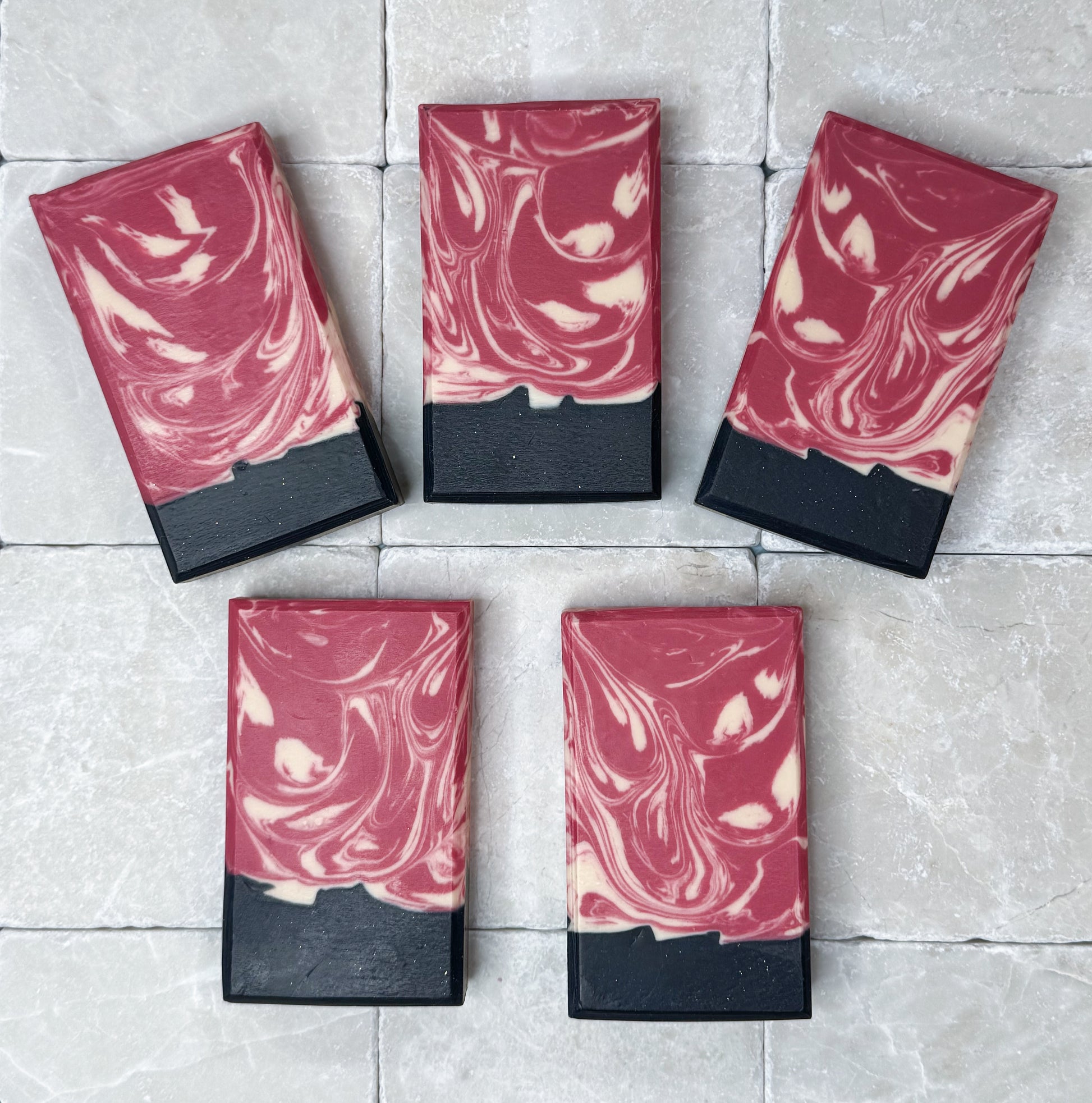 Rose Noir by Happy Hummingbird Soapery: Five rectangular bars with deep red and black marble swirls arranged on a neutral light stone surface.
