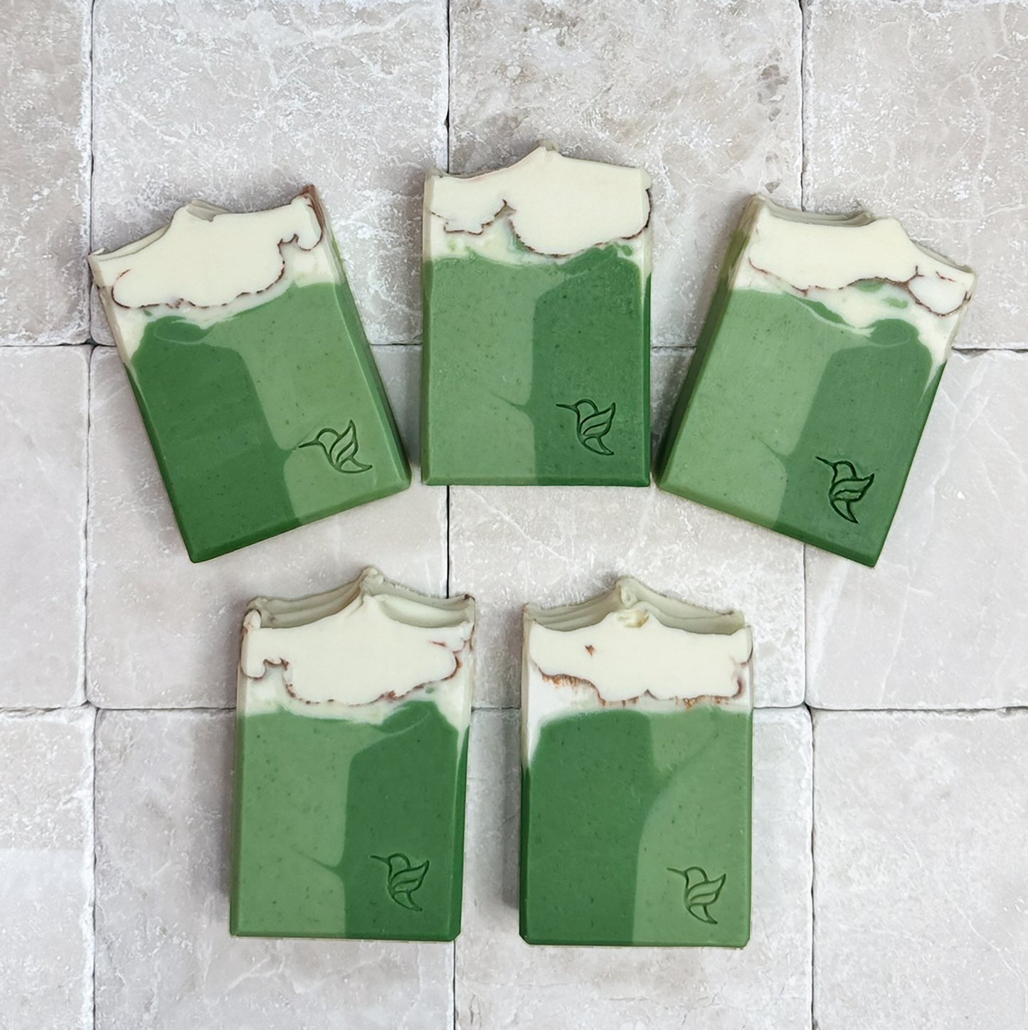 White Tea & Sage Soap by Happy Hummingbird Soapery. Five cream-to-green rectangular bars with hummingbird logos, arranged in a fan on a stone tile background.