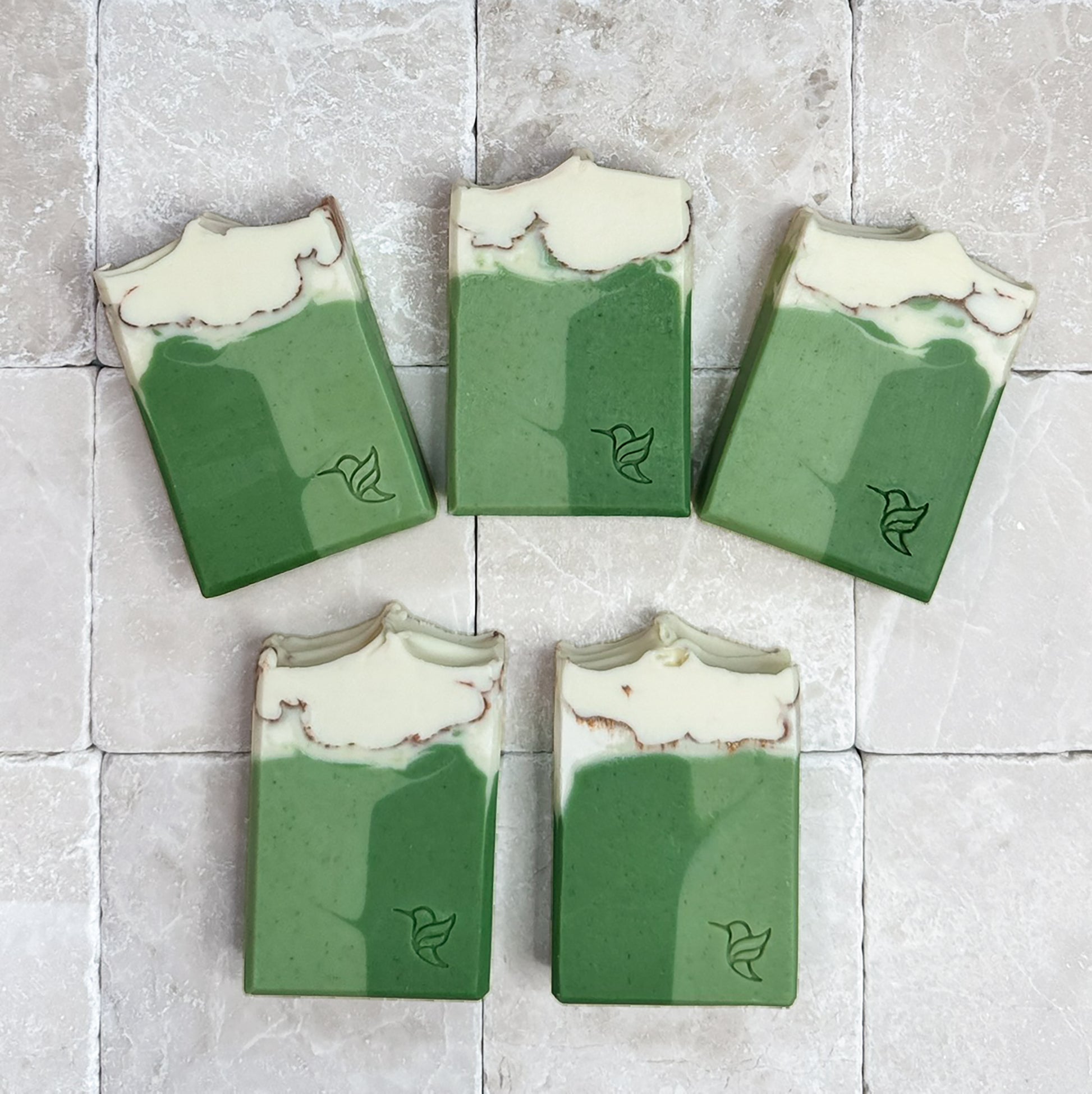White Tea & Sage Soap by Happy Hummingbird Soapery. Five cream-to-green rectangular bars with hummingbird logos, arranged in a fan on a stone tile background.